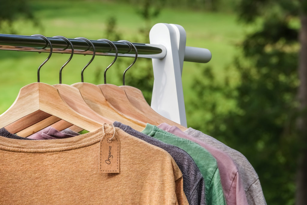 Organic clothes, t-shirts hanging on wooden hangers with green forest, nature in background.